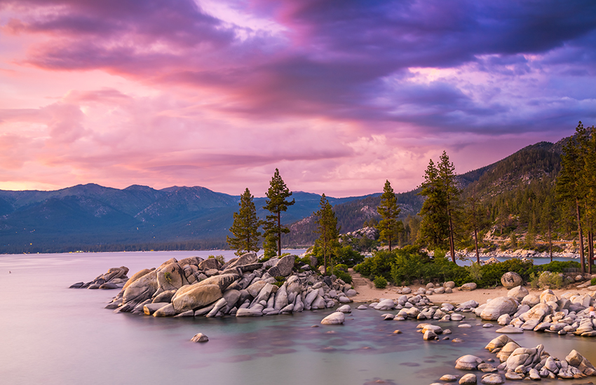 Best Lake Vacations in the U.S. hero image - showing mountains and a rocky beach on a lake